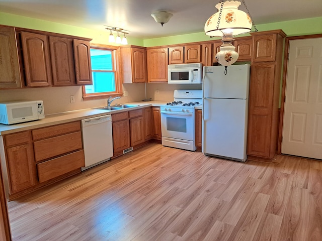 kitchen featuring brown cabinets, white appliances, a sink, and light wood-style floors