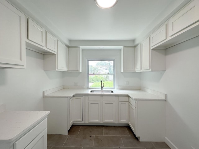 kitchen featuring dark tile patterned flooring, a sink, baseboards, white cabinets, and light countertops