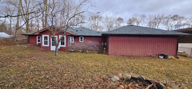 back of house with a shingled roof, a lawn, and fence