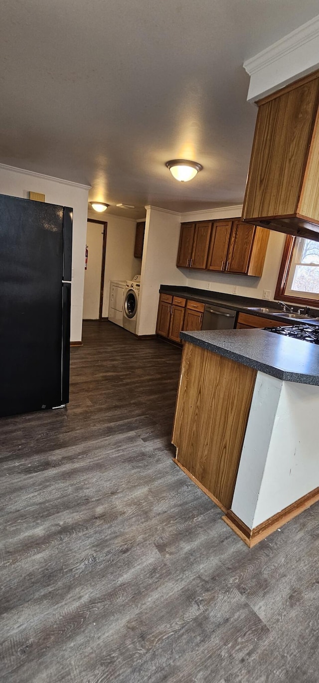 kitchen featuring dark countertops, ornamental molding, brown cabinets, dark wood-style flooring, and freestanding refrigerator