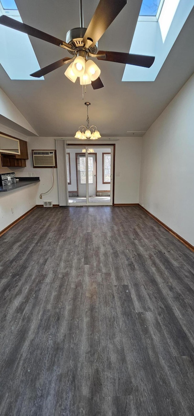 unfurnished living room with vaulted ceiling with skylight, visible vents, baseboards, dark wood-style floors, and a wall mounted air conditioner