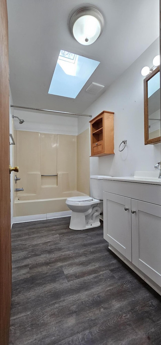 bathroom featuring toilet, a skylight, wood finished floors, vanity, and  shower combination