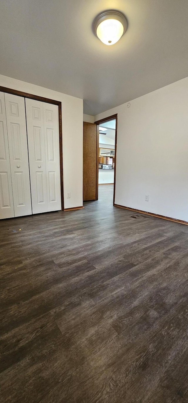 unfurnished bedroom with a closet, baseboards, and dark wood-style flooring