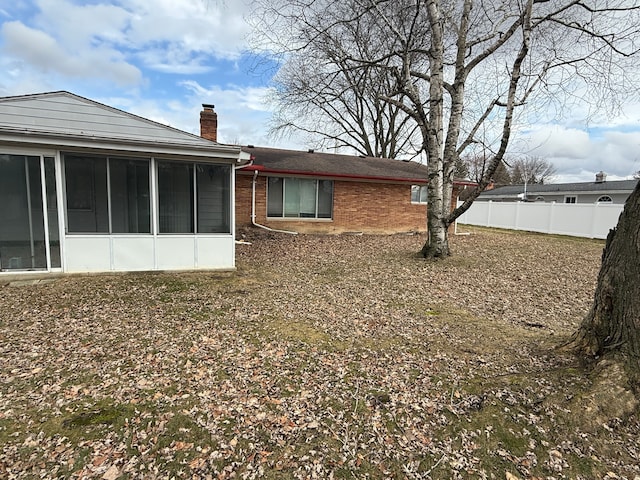 rear view of house with brick siding, a chimney, a sunroom, and fence