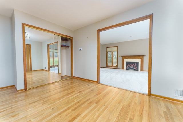 empty room with visible vents, a fireplace, baseboards, and wood finished floors