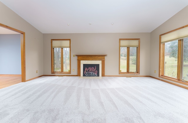 unfurnished living room featuring baseboards, vaulted ceiling, a fireplace with flush hearth, and light colored carpet