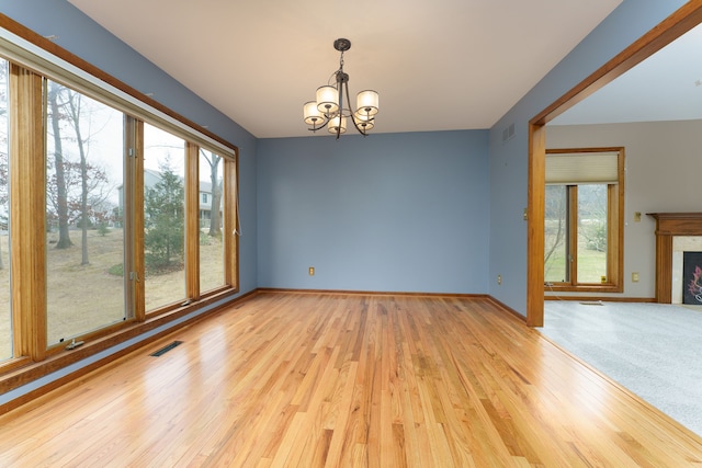 empty room featuring visible vents, a lit fireplace, a wealth of natural light, and an inviting chandelier