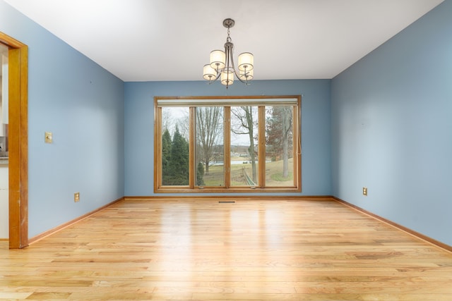 empty room featuring baseboards, wood finished floors, and an inviting chandelier