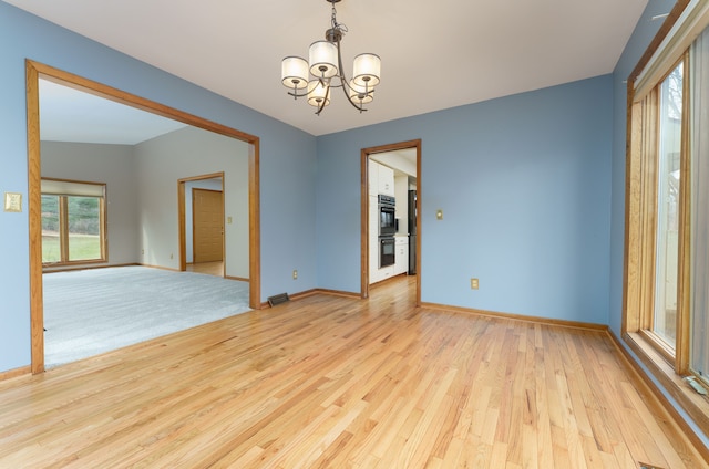 empty room with baseboards, light wood finished floors, and an inviting chandelier