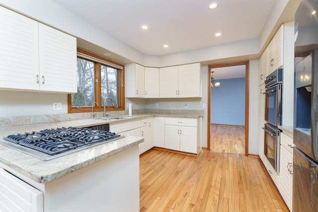 kitchen with white cabinets, light stone counters, light wood-style floors, stainless steel gas cooktop, and a sink