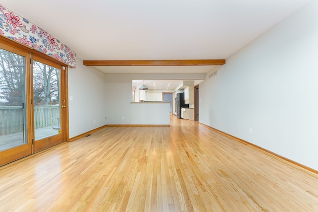 unfurnished living room with light wood-style floors, beam ceiling, and baseboards