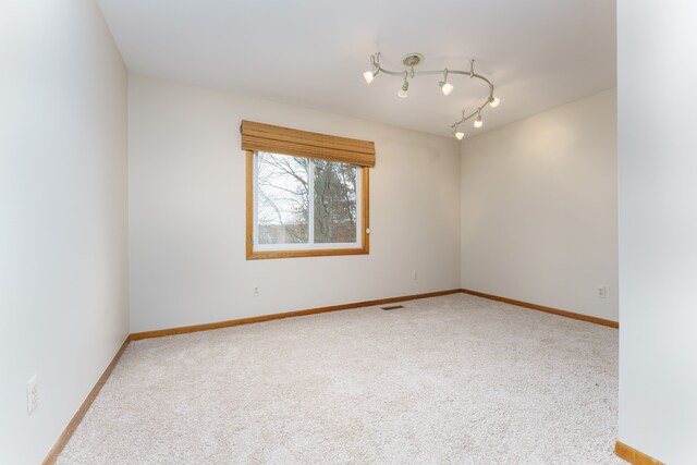 carpeted empty room with track lighting, visible vents, and baseboards