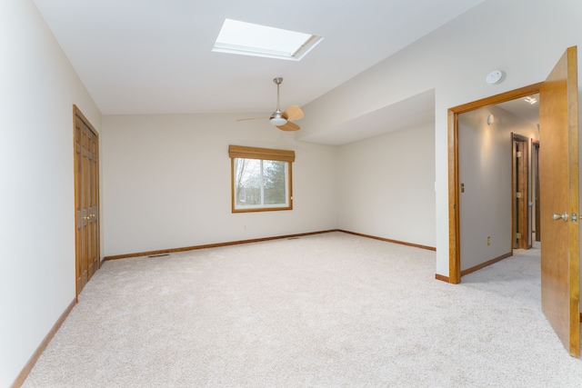 unfurnished room with light carpet, vaulted ceiling with skylight, baseboards, and a ceiling fan