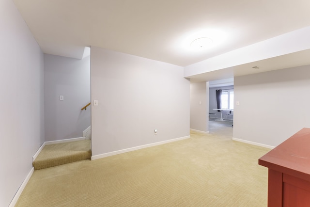 basement featuring light carpet, baseboards, and stairs