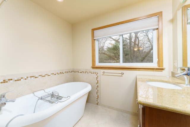 bathroom with baseboards, tile patterned floors, vanity, a freestanding tub, and tile walls