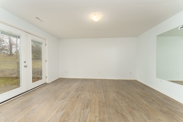 empty room with french doors, light wood finished floors, and baseboards