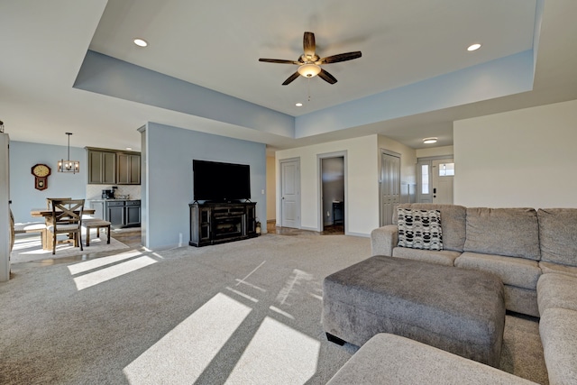 living room with recessed lighting, light carpet, ceiling fan with notable chandelier, baseboards, and a raised ceiling