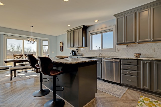 kitchen with a sink, a kitchen island, light stone countertops, dishwasher, and tasteful backsplash