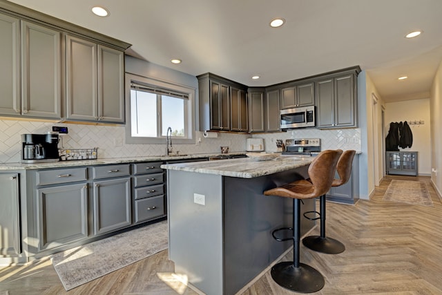 kitchen featuring light stone countertops, recessed lighting, a breakfast bar, appliances with stainless steel finishes, and a center island