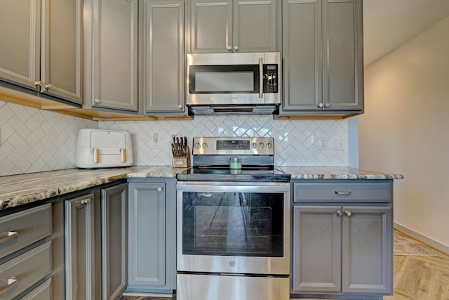 kitchen with baseboards, decorative backsplash, light stone counters, gray cabinets, and stainless steel appliances