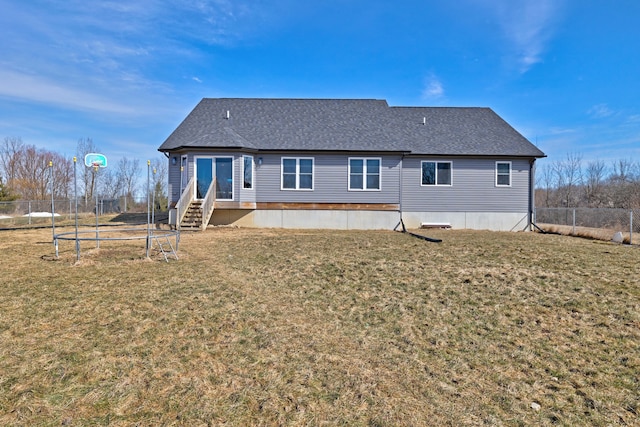 rear view of house with entry steps, roof with shingles, a lawn, and fence