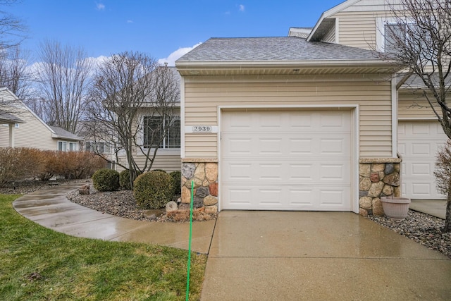 exterior space featuring a garage, stone siding, a shingled roof, and concrete driveway