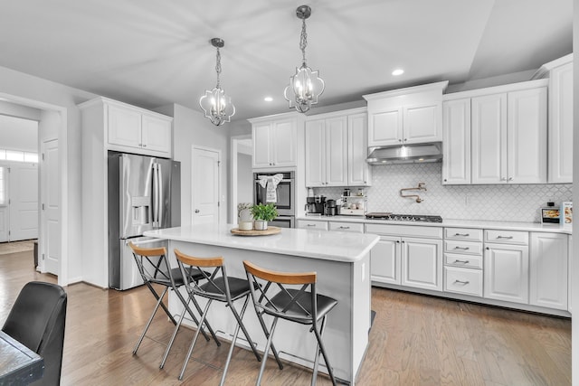 kitchen featuring white cabinets, appliances with stainless steel finishes, wood finished floors, light countertops, and under cabinet range hood