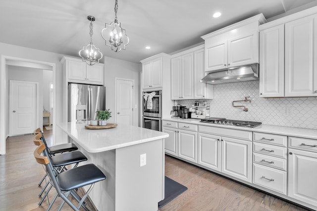 kitchen featuring under cabinet range hood, stainless steel appliances, white cabinetry, a kitchen breakfast bar, and light countertops