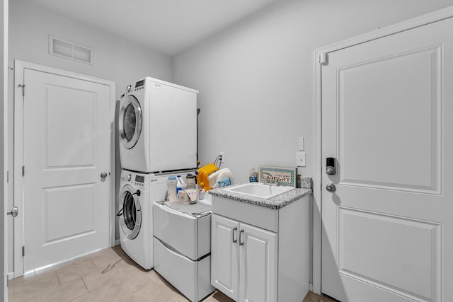 washroom with cabinet space, light tile patterned floors, visible vents, stacked washer / dryer, and a sink