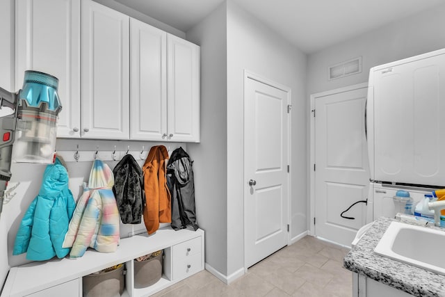 mudroom with light tile patterned flooring, a sink, visible vents, baseboards, and stacked washer and clothes dryer