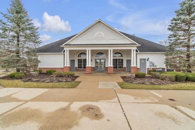 view of front of house featuring brick siding, a shingled roof, a porch, and french doors