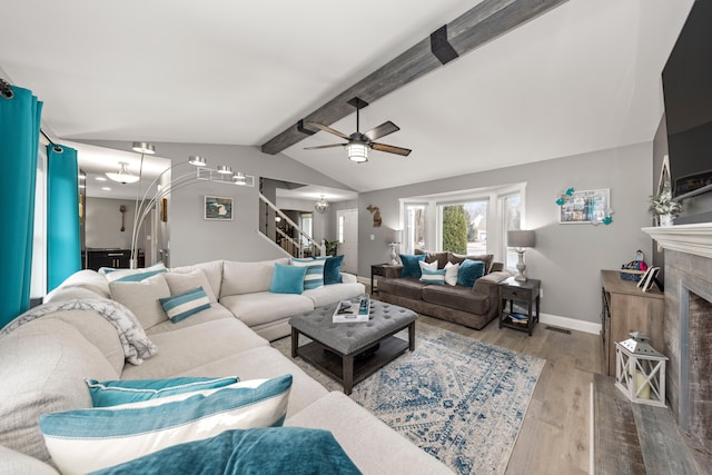 living room featuring lofted ceiling with beams, wood finished floors, a tile fireplace, baseboards, and stairs