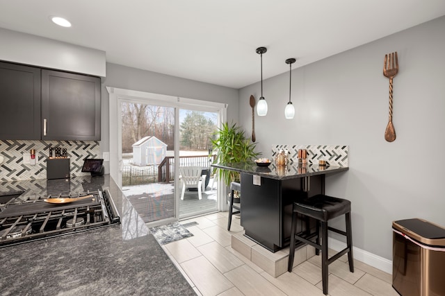 kitchen featuring tasteful backsplash, baseboards, decorative light fixtures, gas stovetop, and a kitchen bar