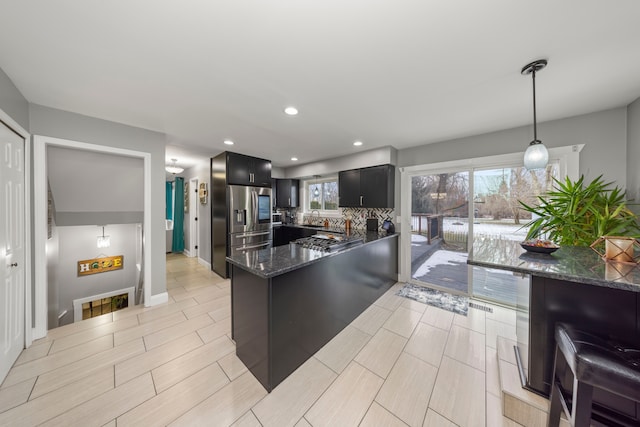 kitchen with stainless steel fridge, dark stone counters, dark cabinets, backsplash, and recessed lighting