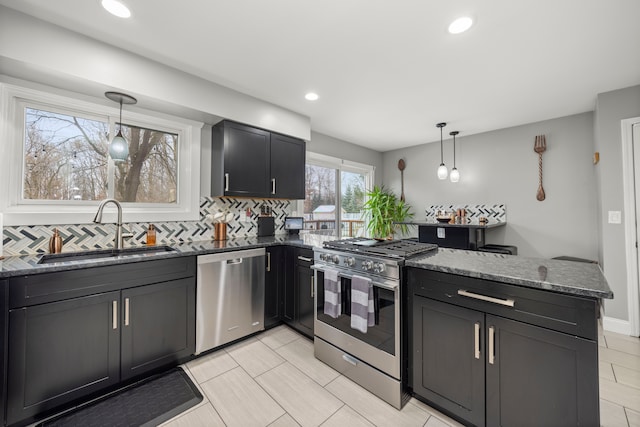 kitchen featuring stainless steel appliances, decorative backsplash, a sink, dark stone counters, and a peninsula