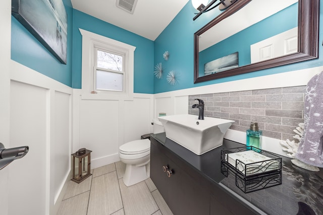 bathroom with toilet, a wainscoted wall, visible vents, and vanity