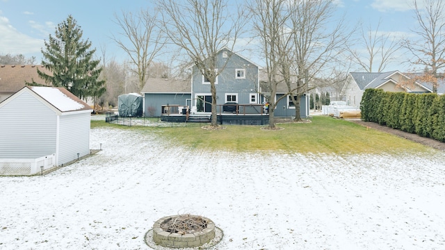 snow covered back of property featuring a deck, a lawn, and an outbuilding