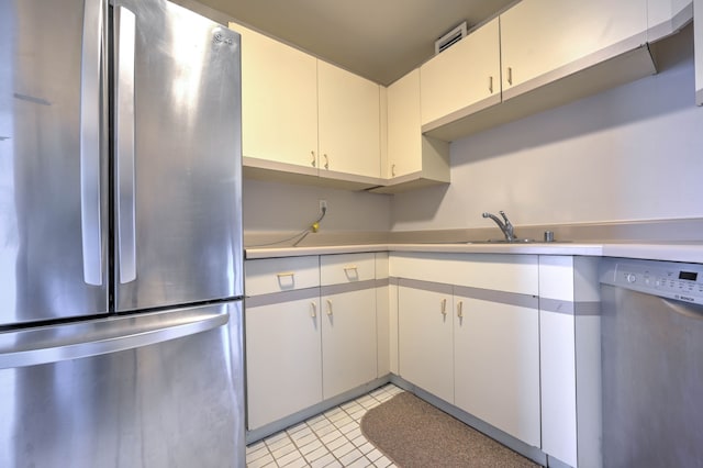 kitchen with appliances with stainless steel finishes, white cabinets, light countertops, and a sink