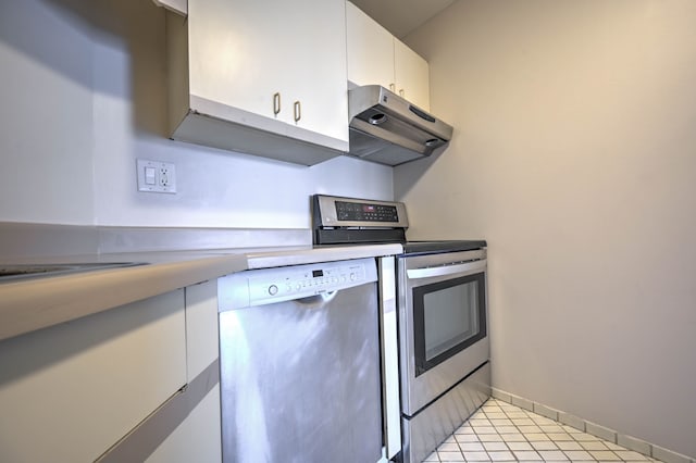 kitchen featuring light tile patterned flooring, under cabinet range hood, stainless steel appliances, white cabinetry, and baseboards