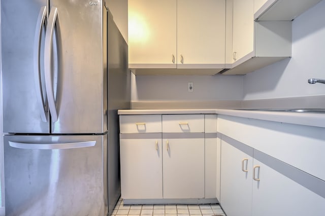 kitchen with light countertops, a sink, freestanding refrigerator, and white cabinets