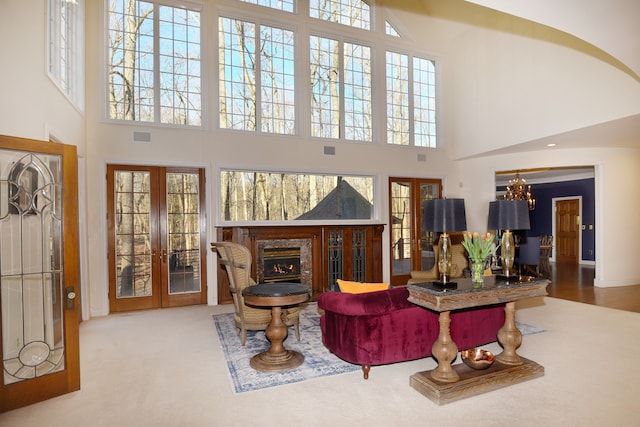 carpeted living room featuring a high end fireplace, visible vents, french doors, and a towering ceiling