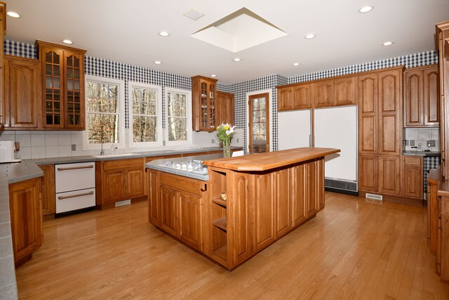 kitchen with light wood finished floors, a center island, a skylight, brown cabinetry, and white appliances