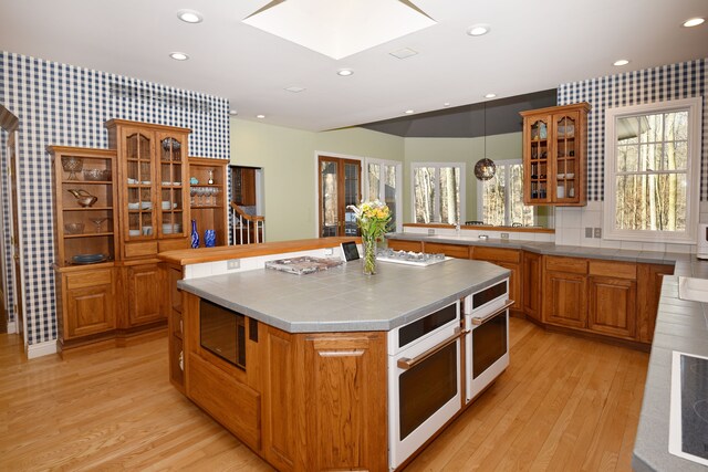 kitchen featuring brown cabinetry, stainless steel microwave, a skylight, and light wood-type flooring