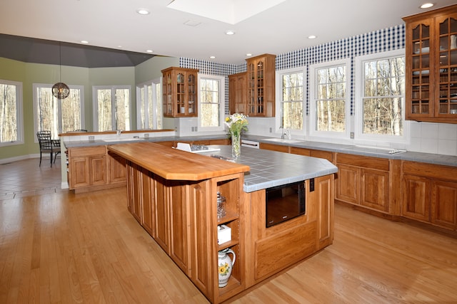 kitchen with a sink, a peninsula, black microwave, light wood finished floors, and glass insert cabinets