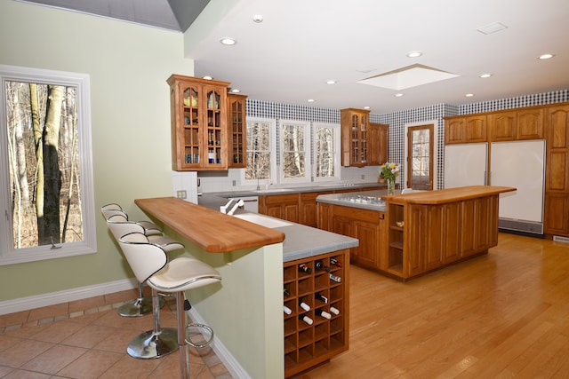 kitchen with open shelves, a kitchen island, white fridge, brown cabinetry, and glass insert cabinets