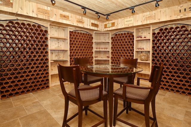 wine cellar featuring wooden walls, rail lighting, wood ceiling, and stone finish flooring