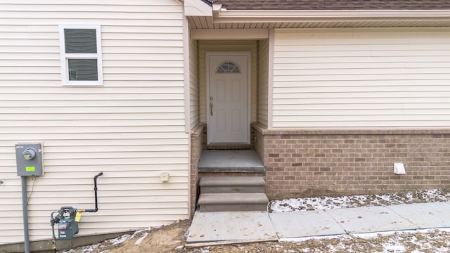 doorway to property featuring a shingled roof and brick siding