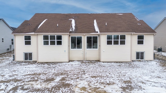 snow covered property featuring a shingled roof and central AC unit