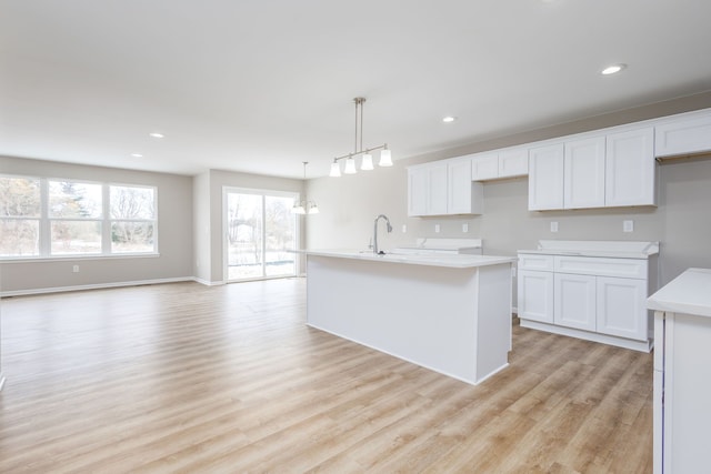 kitchen with a center island with sink, light wood-style flooring, light countertops, white cabinetry, and recessed lighting