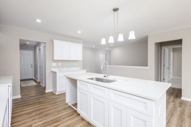 kitchen with white cabinetry, a sink, decorative light fixtures, and light wood finished floors